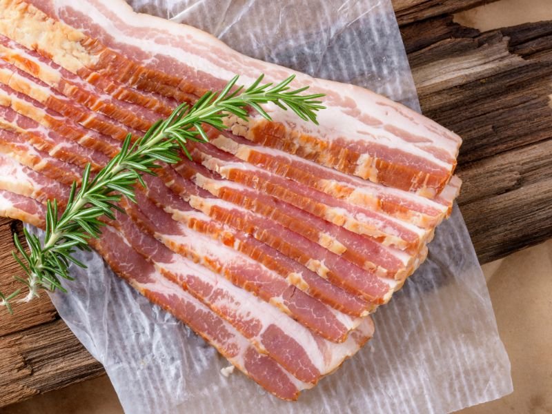 thick slices of bacon on waxed paper with sprig of rosemary