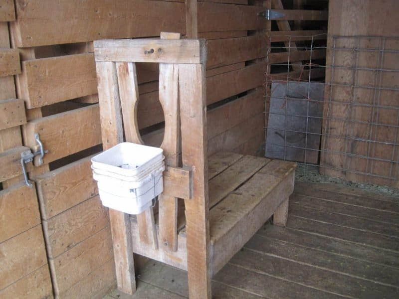 White ceramic neti pot on wooden surface with salt water jar in background.