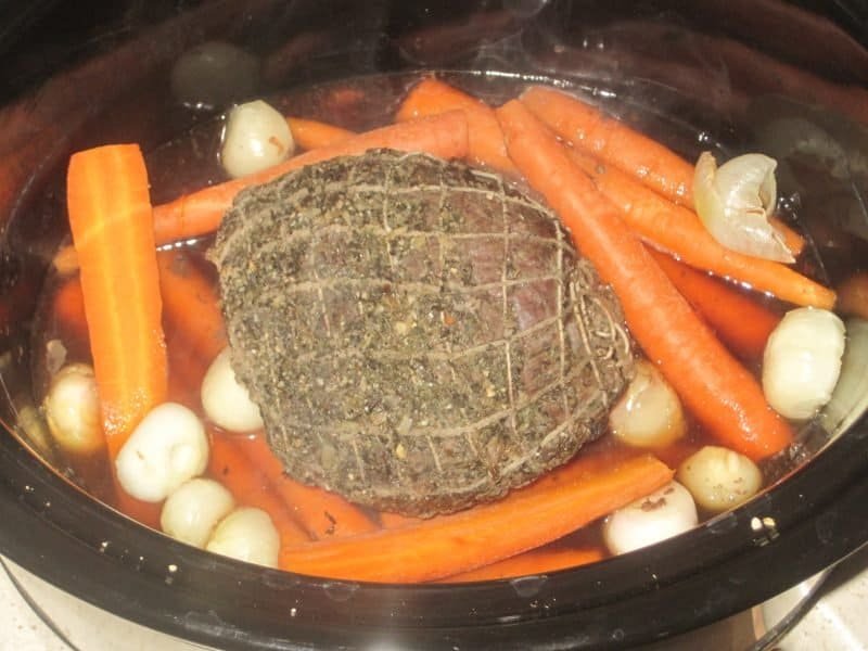 Adding Carrots and Potatoes to Roast in a black crockpot