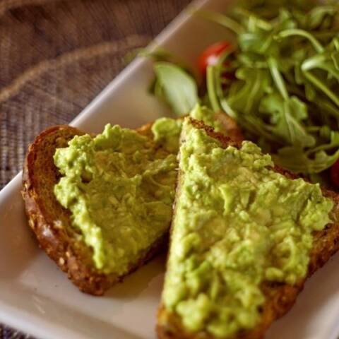 fresh avocado spread on whole wheat toast on a square white plate