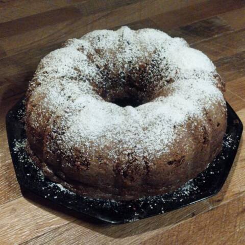 Freshly baked homemade chocolate cake dusted with powdered sugar on a black plate