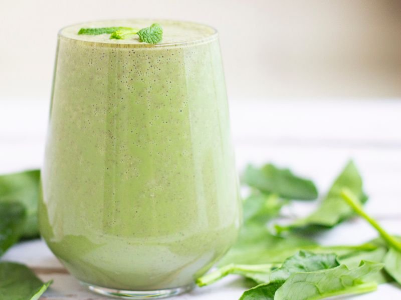 fresh green protein powder smoothie in a glass on a kitchen counter