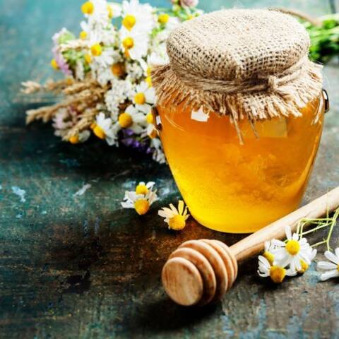 simple jar of honey with a bouquet of small aster flowers and a honey swirl stick
