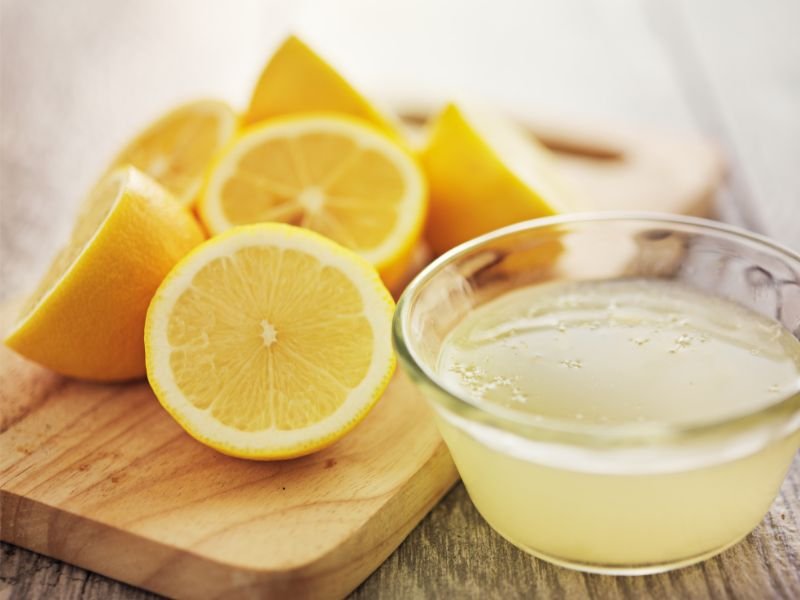 A cutting board shows halved and quartered lemons next to a small bowl of fresh lemon juice. This setup gives a hint on making an easy lemon vinaigrette or homemade dressing.