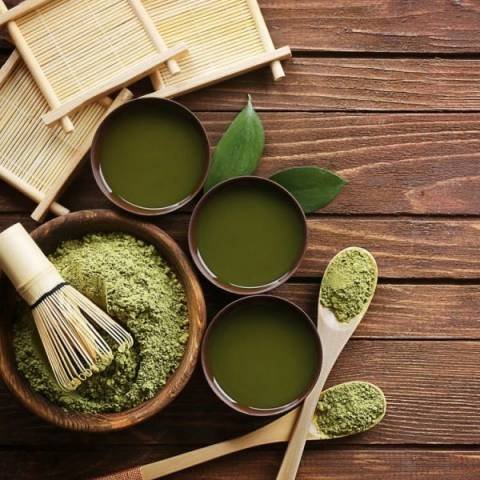 Matcha Green Tea powder and cups of green tea on a wooden table