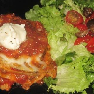 a piece of Mexican-Lasagna on a black plate ready to serve with a fresh green salad sprinkled with cherry tomatoes and black olives