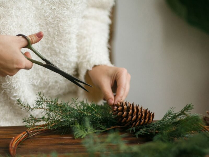 woman using scissors to make a pinecone and pine bough home wreath