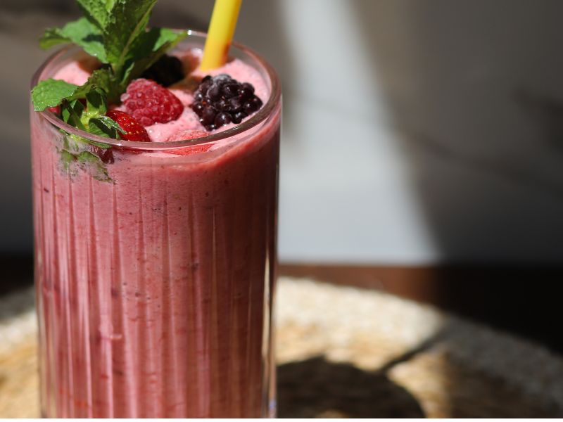 blackberry smoothie in a tall glass with a yellow straw