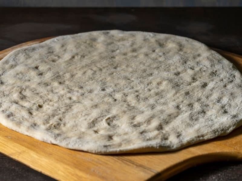 spreading out homemade dough on a wooden pizza paddle