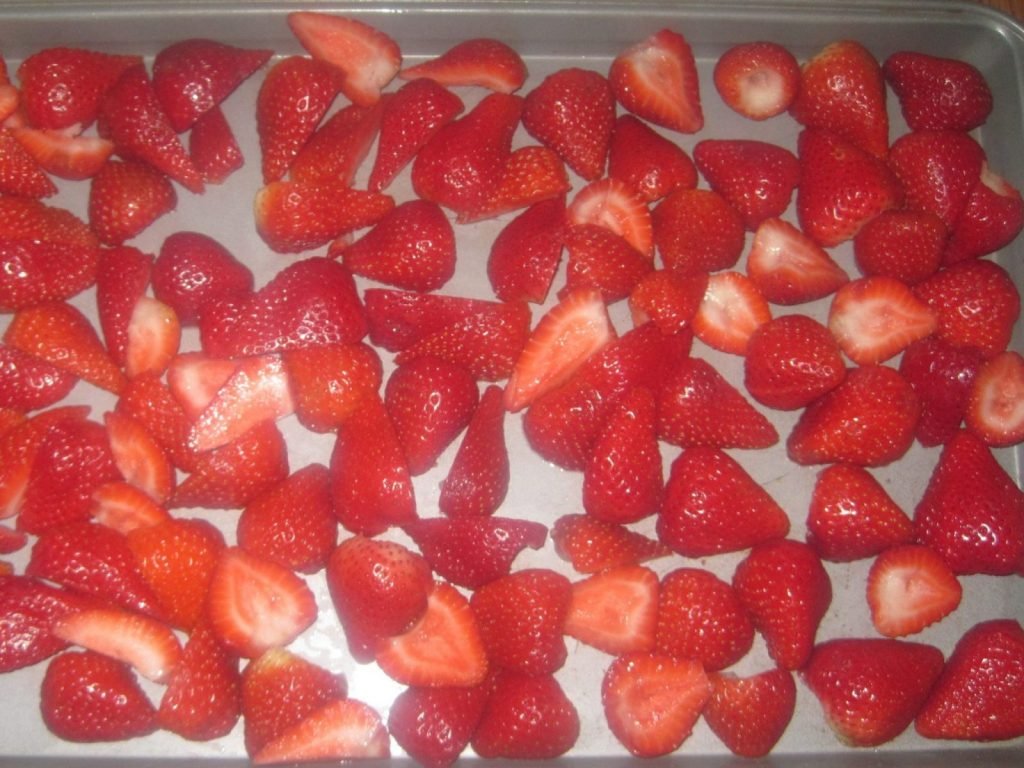 fresh strawberries halves on a sheet ready to freeze