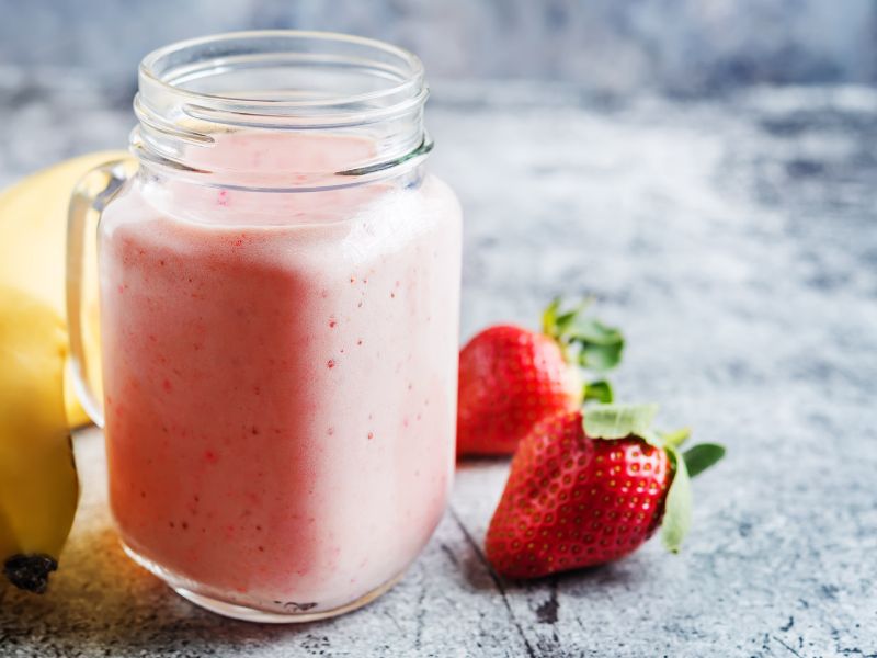 strawberry smoothie in a canning jar on a table with strawberries and a banana