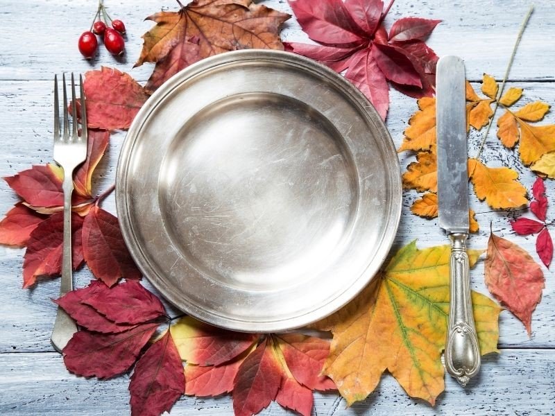pewter plate and vintage silverware on a bed of autumn colored leaves makes a rustic place setting on a whitewashed plank table