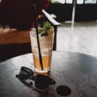 a tall glass of Tulsi Tea with a straw on a table by a pair of sunglasses