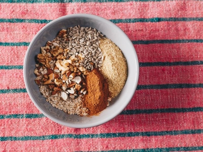 nuts, seeds, oats meal and cinnamon in a breakfast bowl on a striped tablecloth