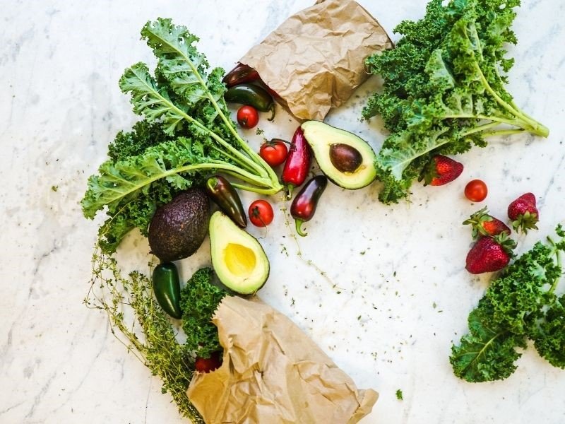 fresh fruits and vegetables on a marble slab with a simple brown paper bag