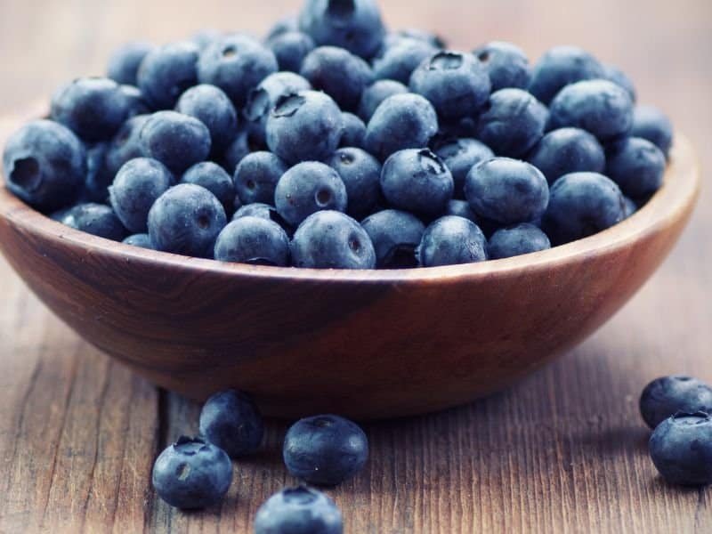 A wooden bowl filled with fresh blueberries sits on a wooden surface, illustrating how to freeze blueberries.