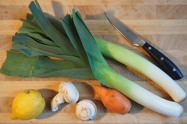 fresh garden leeks, lemon, mushrooms and a small carrots on a wooden cutting boards